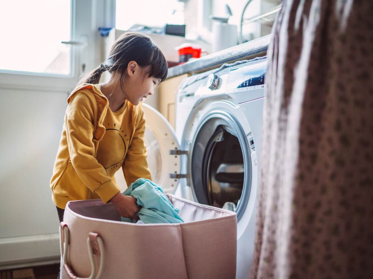 Little girl unloading the washing machine while helping her mom with laundry at home