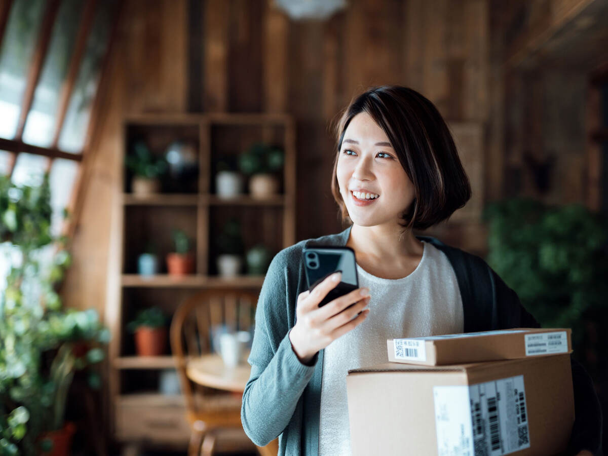 Person holding cellphone and packages in their home