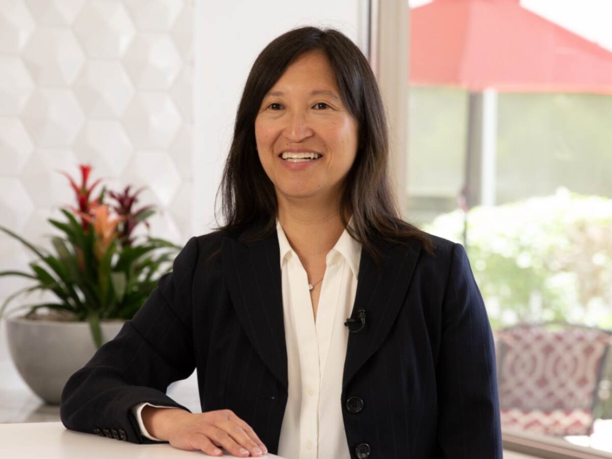 Cynthia Ho in black jacket and white shirt sitting at table. 