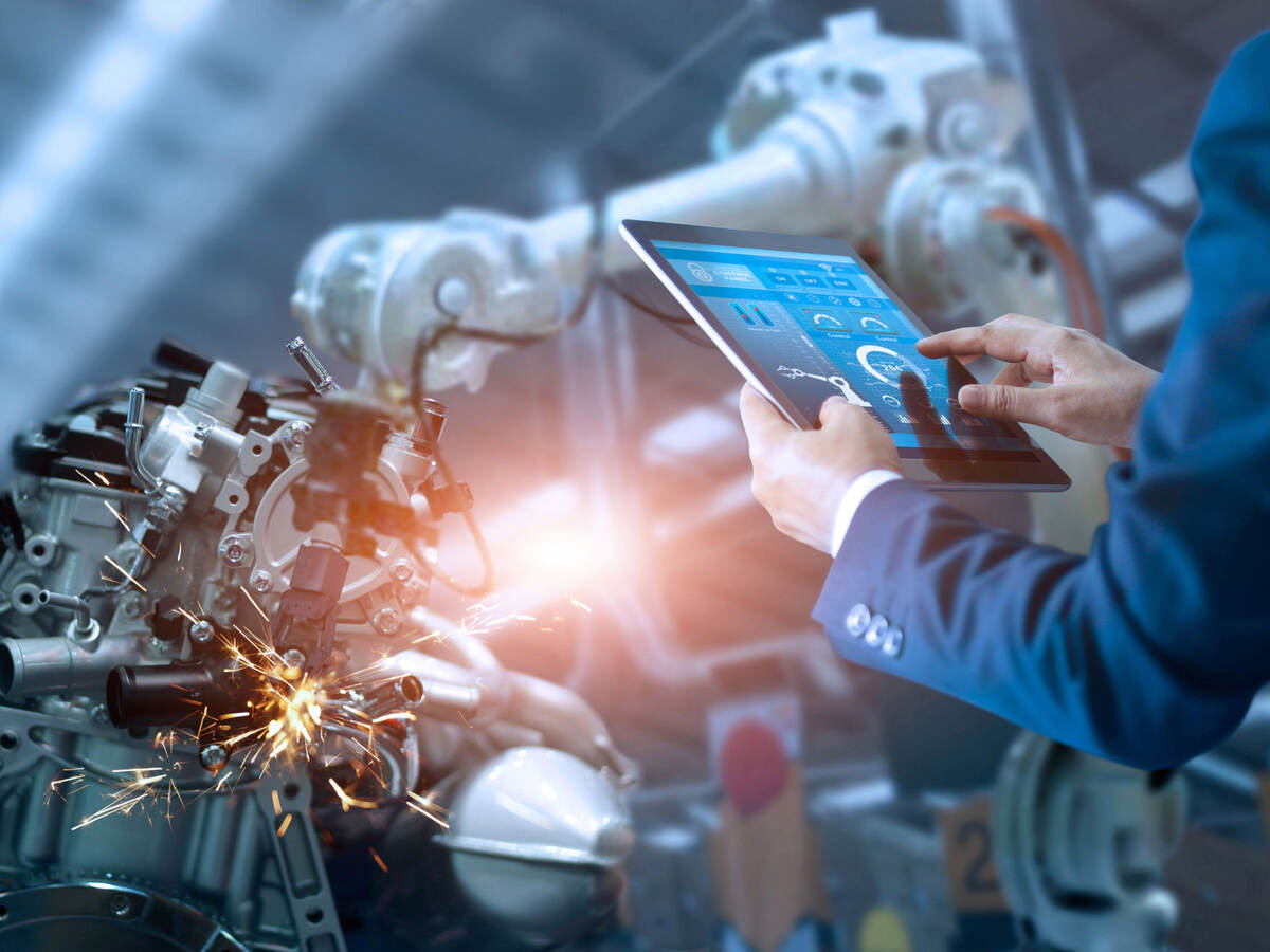 Person using tablet to control robotic arm in a factory