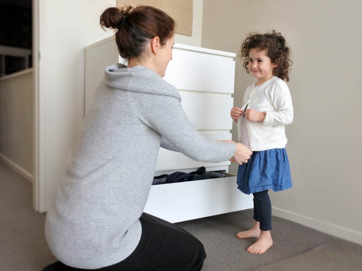 Young girl is getting dressed up with the help of her mother.