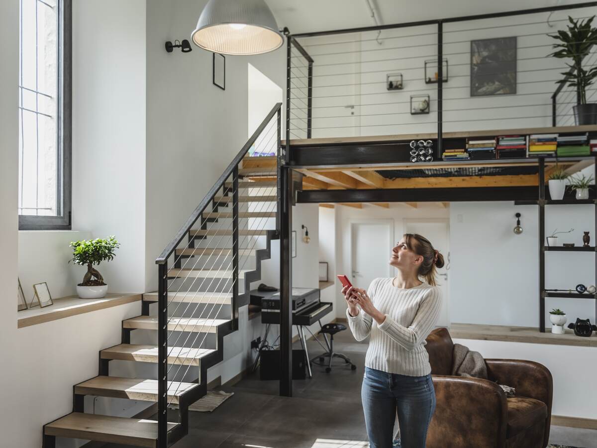 Young woman controlling smart home functions through mobile phone at modern home.