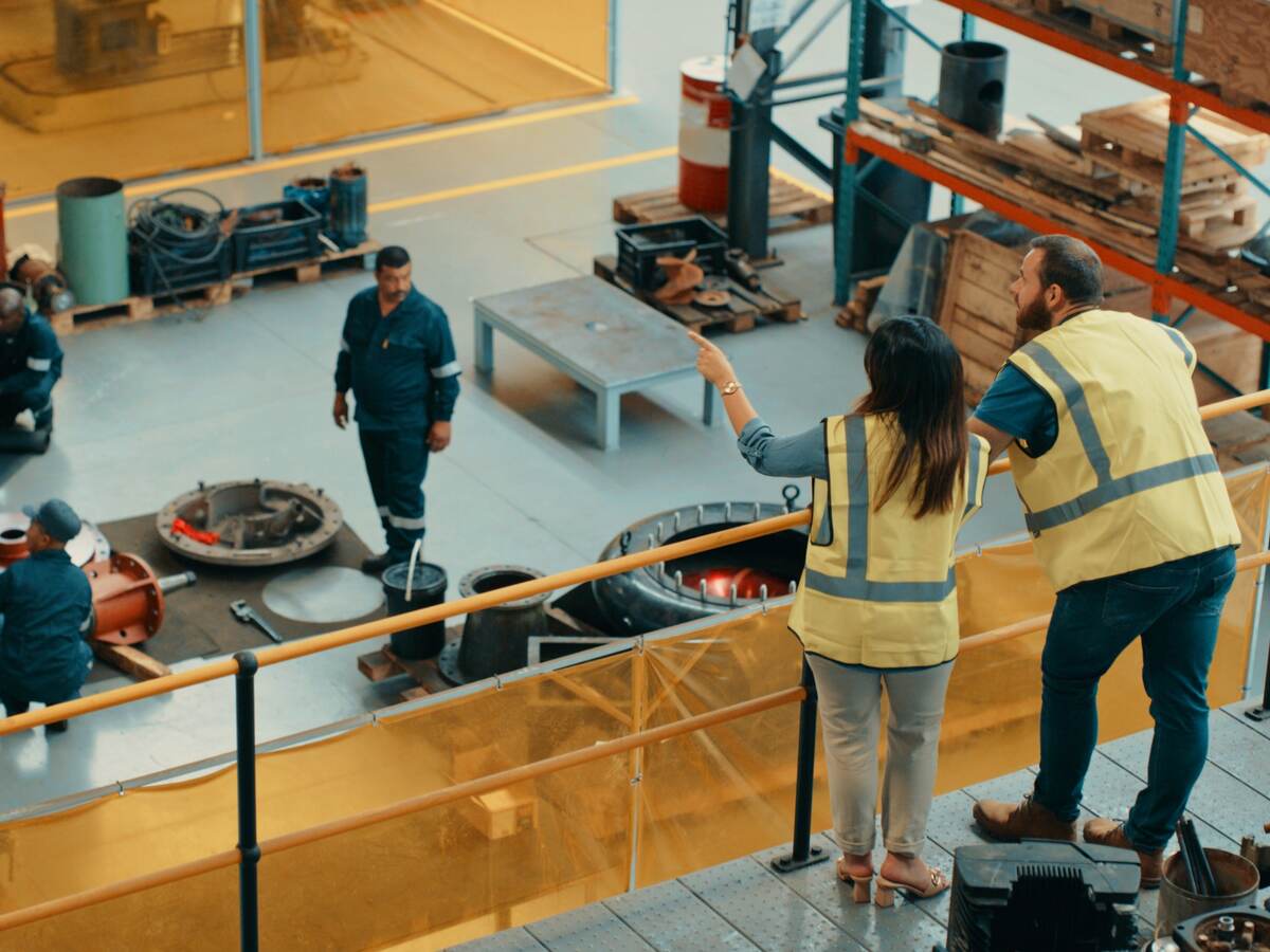 Managers at a manufacturing warehouse factory watching workers inside a capability building workshop.