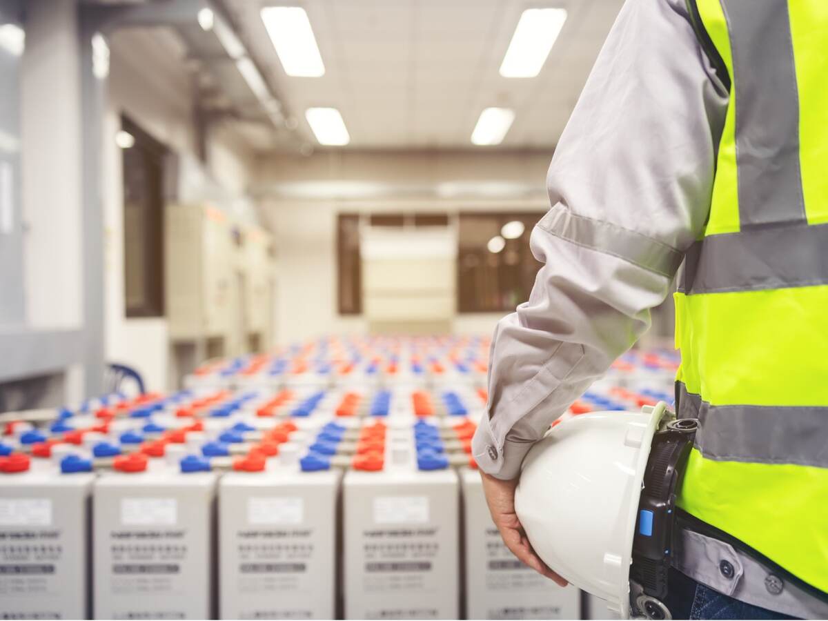 rows of batteries in front of worker with yellow safety vest 