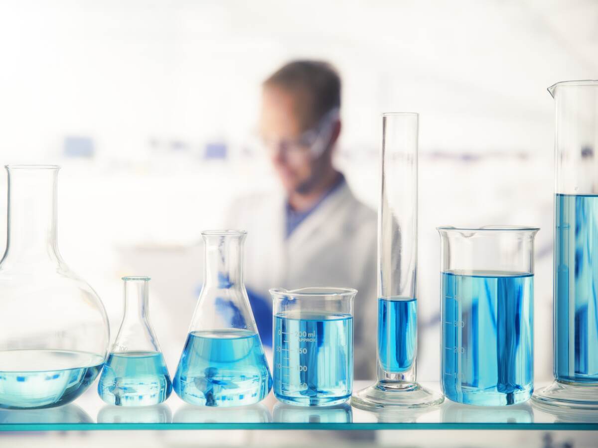 Close up of various solutions in beakers on shelf in lab.