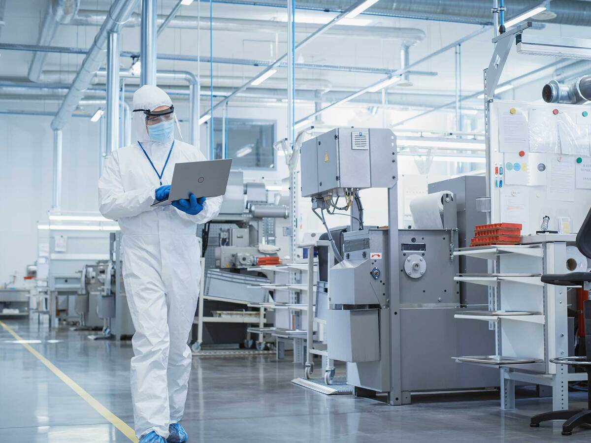 Person wearing PPE and walking through a lab while looking at a laptop