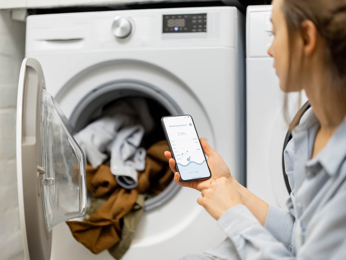 Woman controls washing machine with a smartphone.