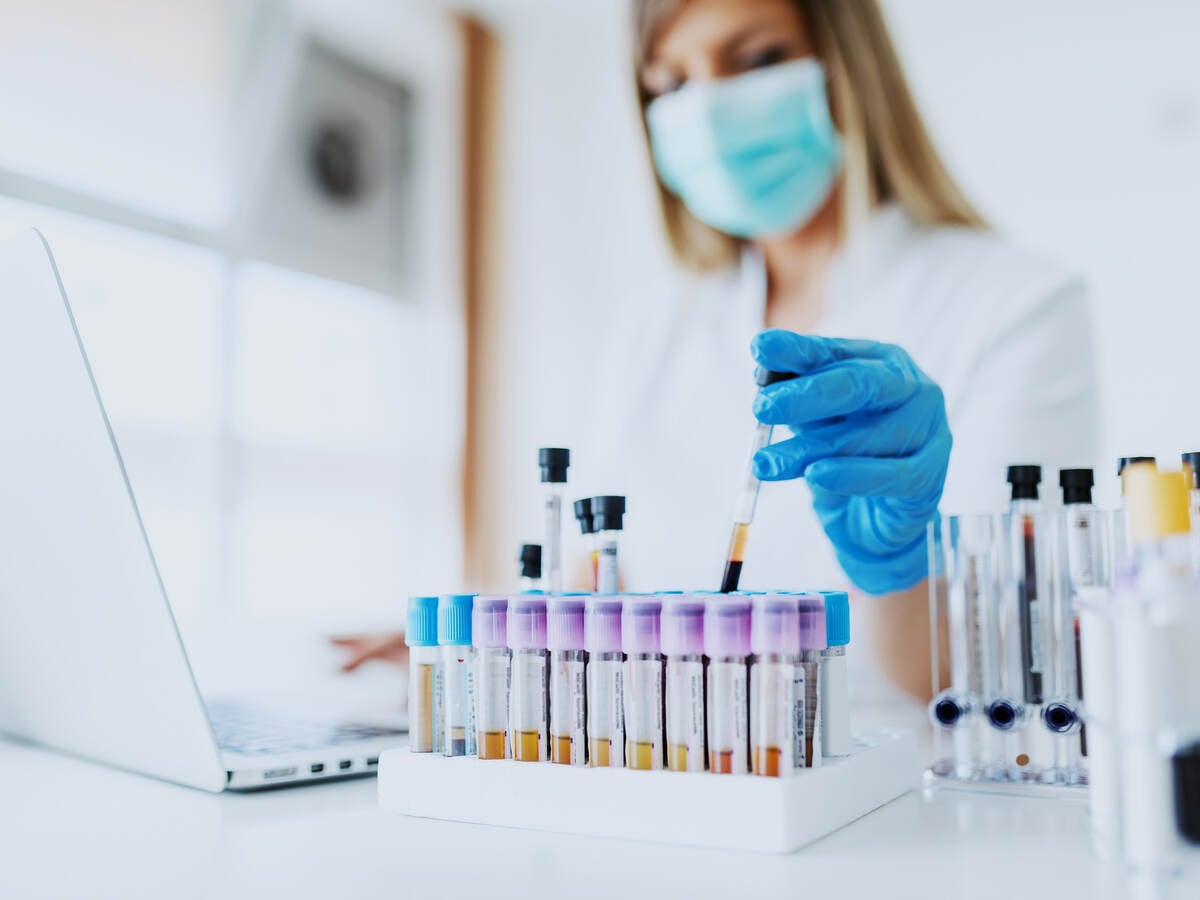 Close up of lab assistant holding test tube while wearing a lab coat, mask and rubber gloves