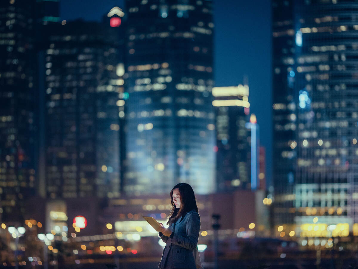 Person using a tablet at night while outside in a large city
