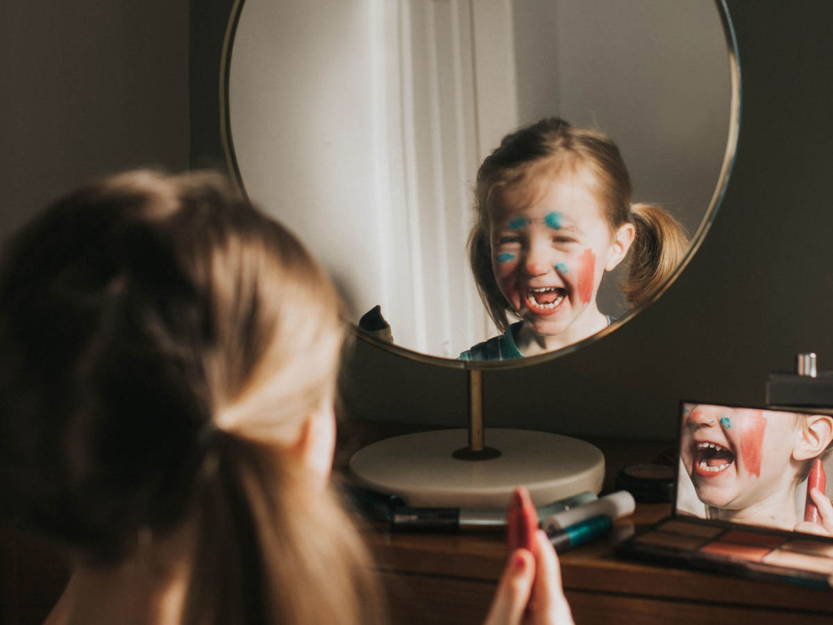 A child playing with makeup and looking in a mirror, laughing