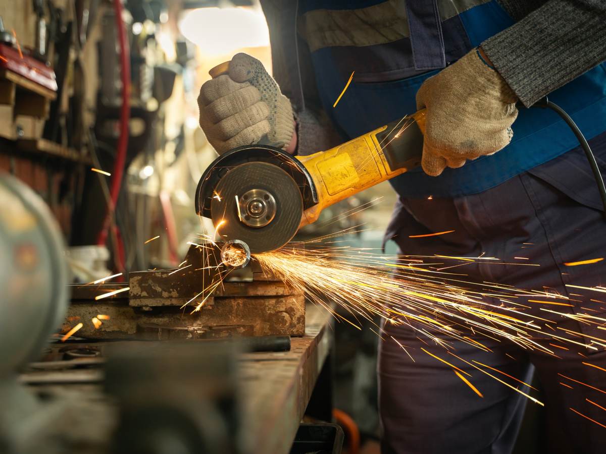 Metalworker using handheld circular saw on metal pipe as sparks fly.