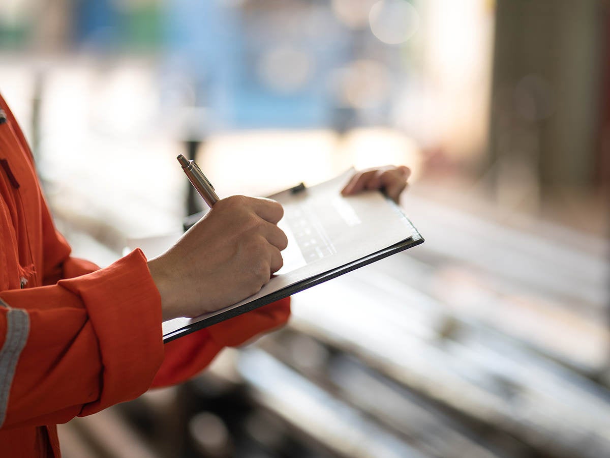 Writing on safety checklist document during safety audit and inspection.