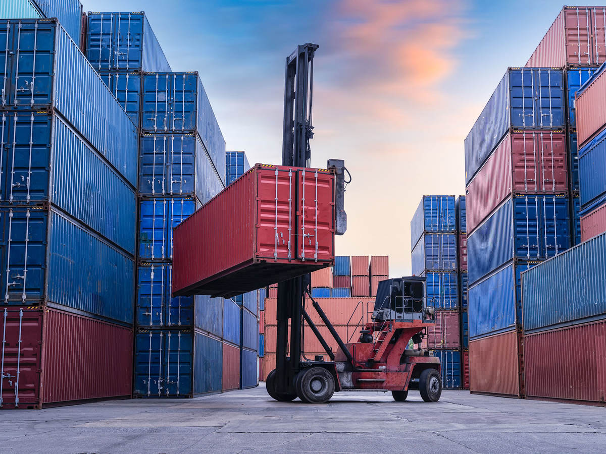 Forklift truck handling cargo shipping container box in logistic shipping yard with cargo container stack