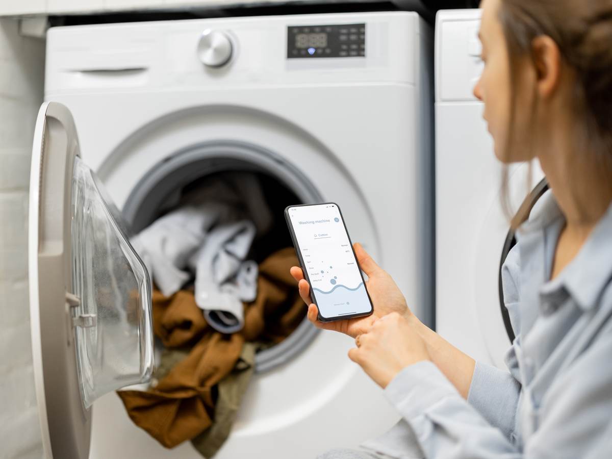 Woman controls washing machine with a smartphone