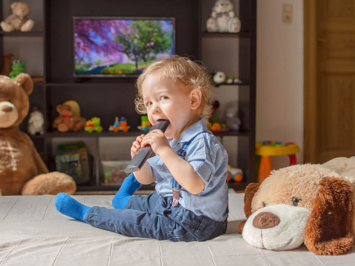 Toddler sitting while chewing on a tv remote