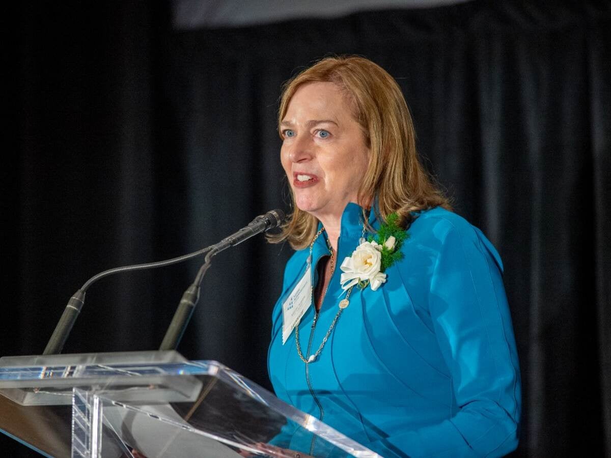 Jennifer Scanlon speaks at podium dressed in teal. 