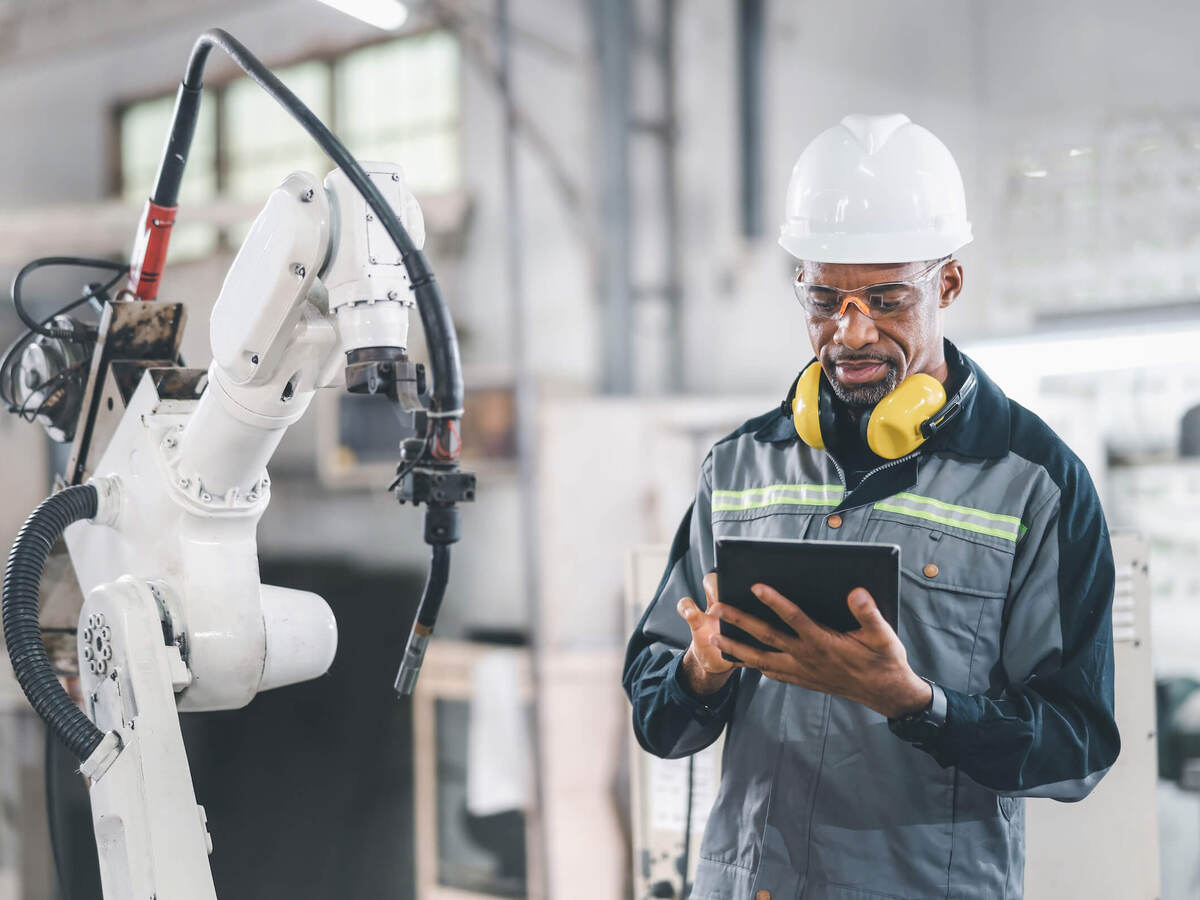 Engineer working on a tablet in front of a mechanical arm in a factory