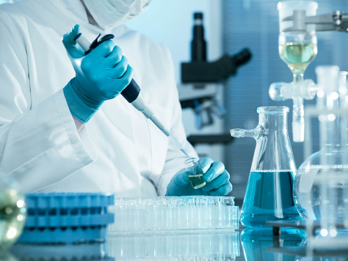 A laboratory technician using a pipette, testtubes, and flasks with blue liquid