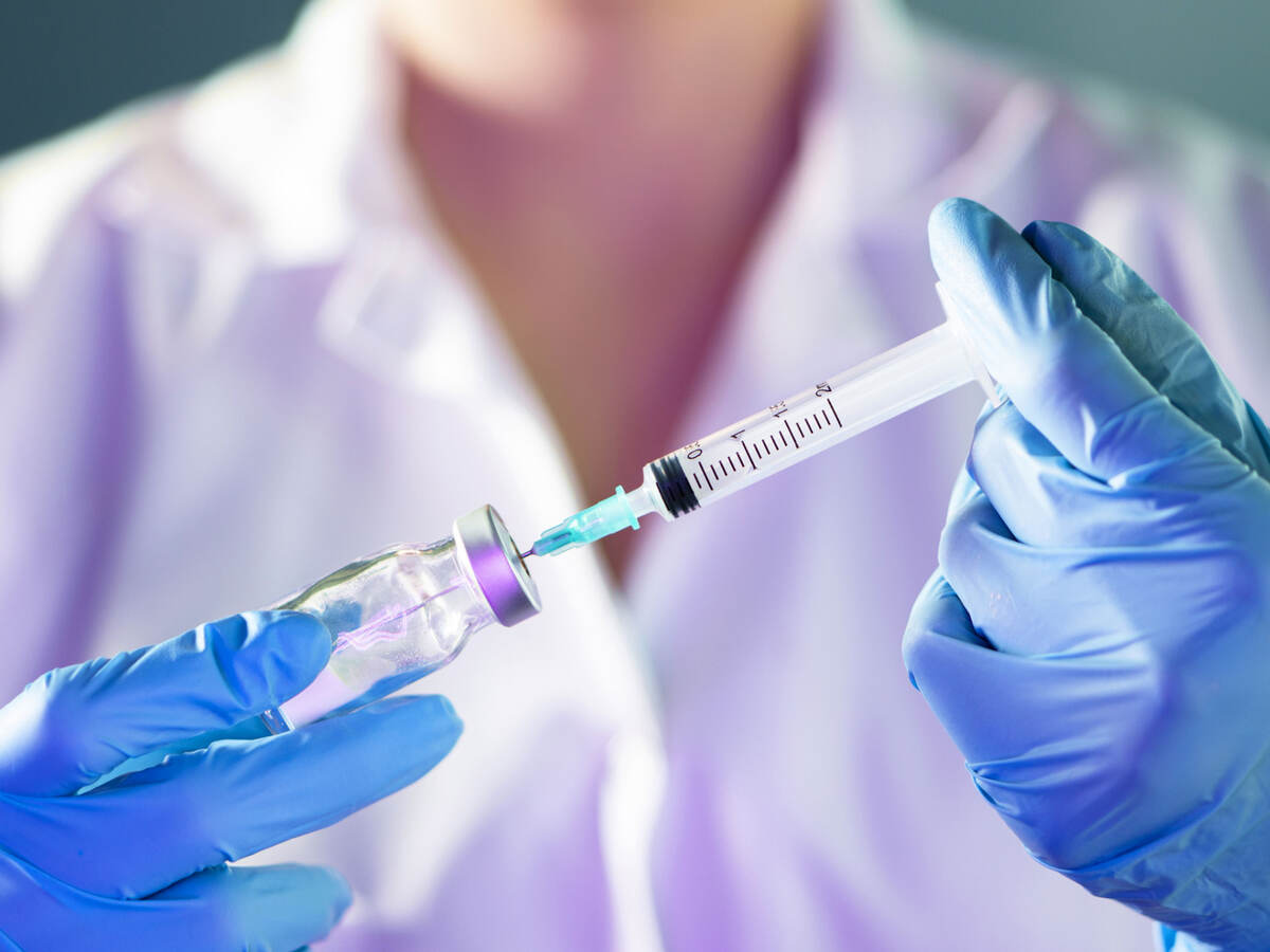 Closeup of a medical professional's hands in blue gloves holding syringe and vial.