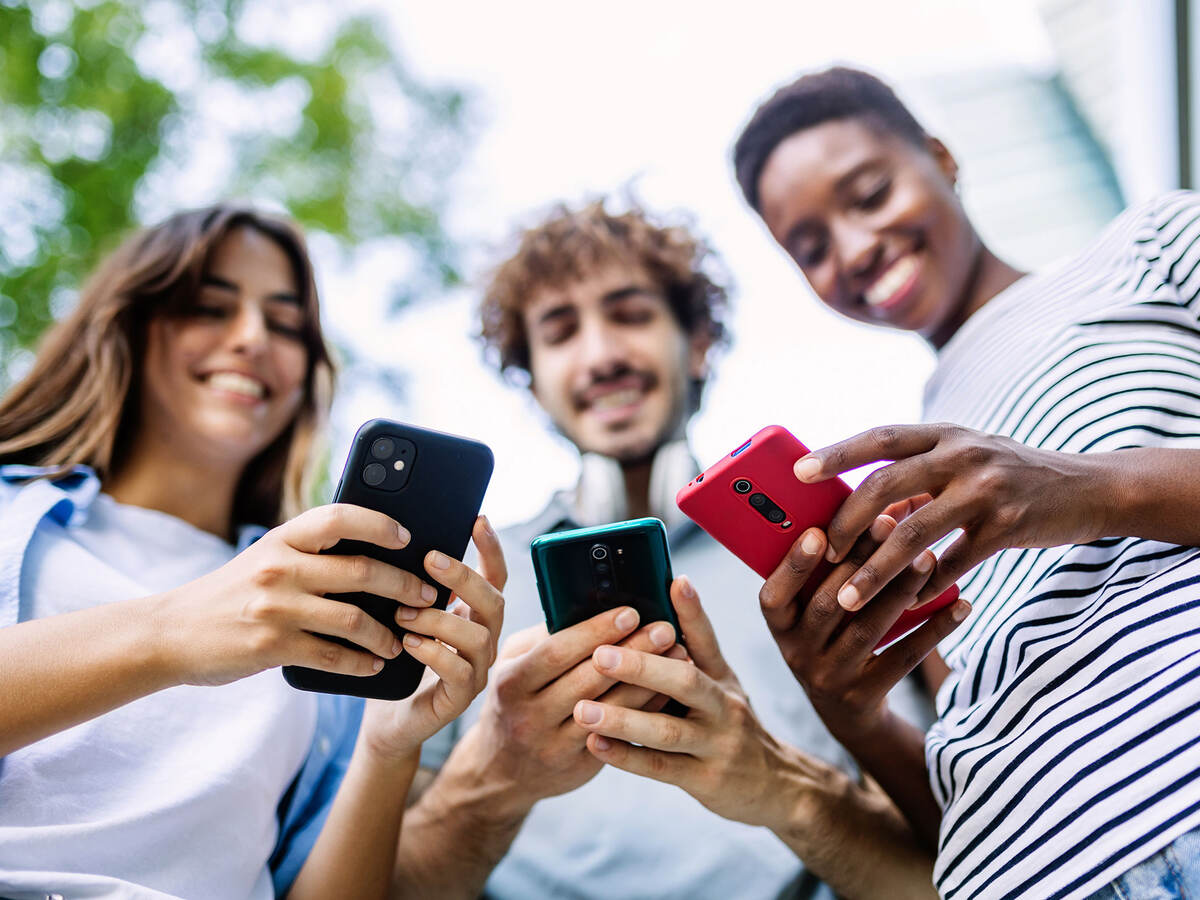 Three smiling friends outdoors and holding cellphones