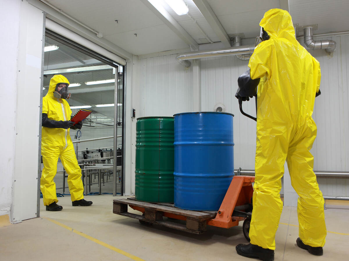 Two people wearing protective clothing and working with a chemical barrel delivery