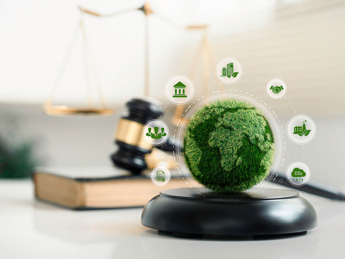 A small depiction of a world sitting on a wooden block with sustainability icons surrounding it, along with a gavel and gold scales in the background