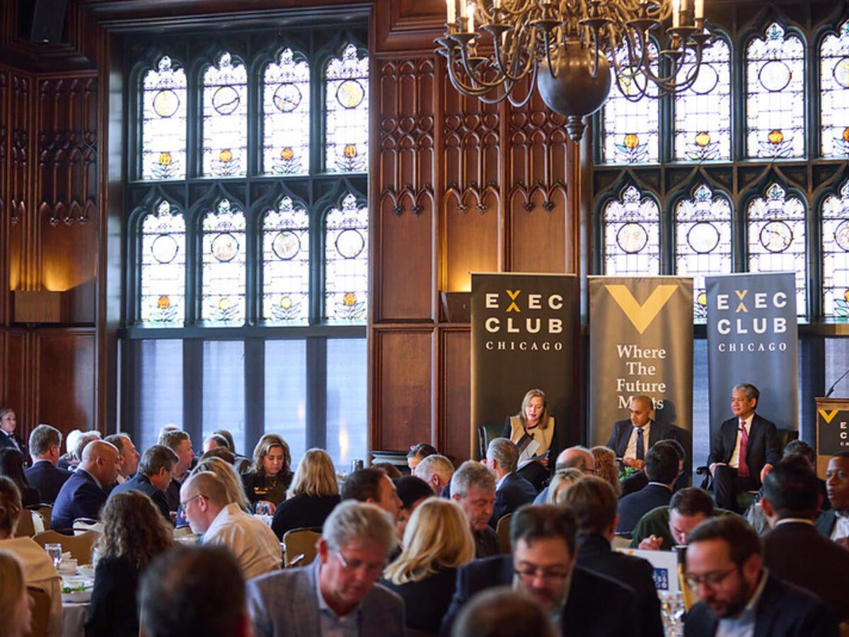 Scanlon and panelists talk in front of stained-glass windows as audience listens. 