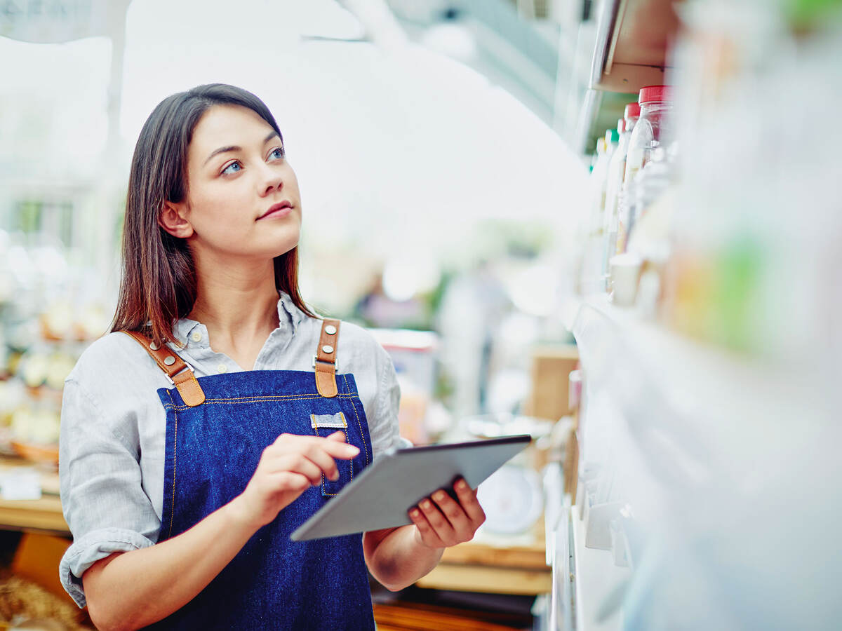 A young person holding a tablet and doing inventory in a store