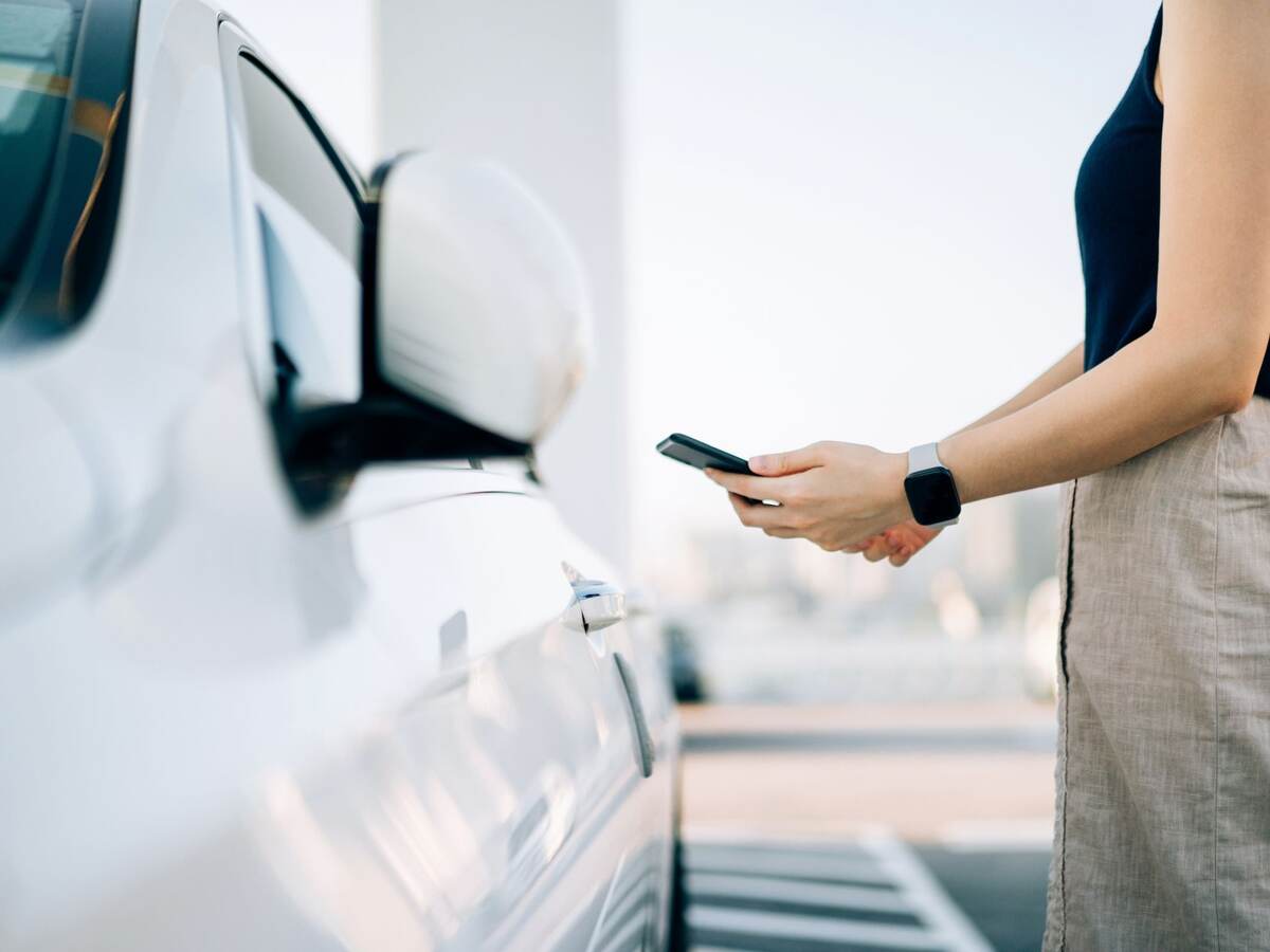 Close up of young Asian woman using mobile app device on smartphone to unlock the doors of her car in a car park.