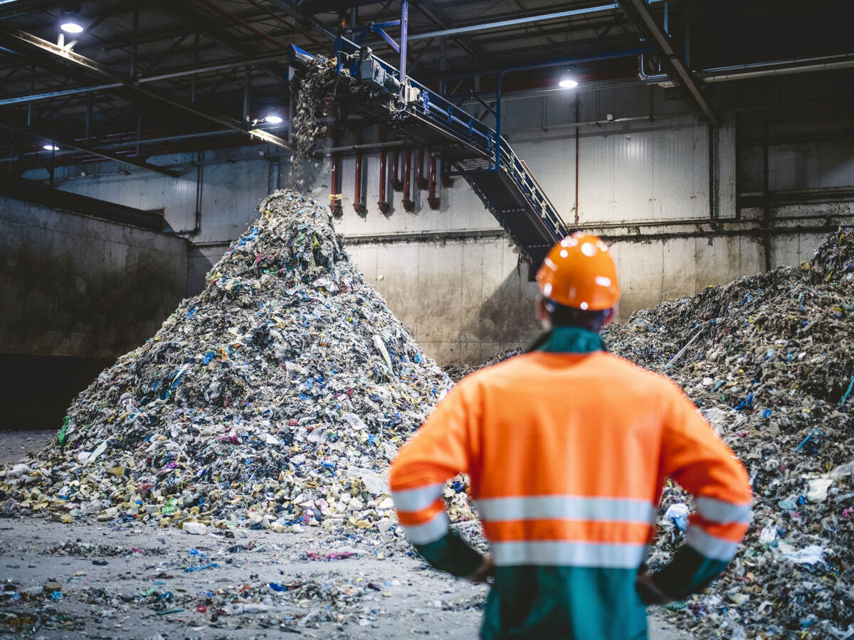 A worker wearing orange PPE and looking at recycling at a facility