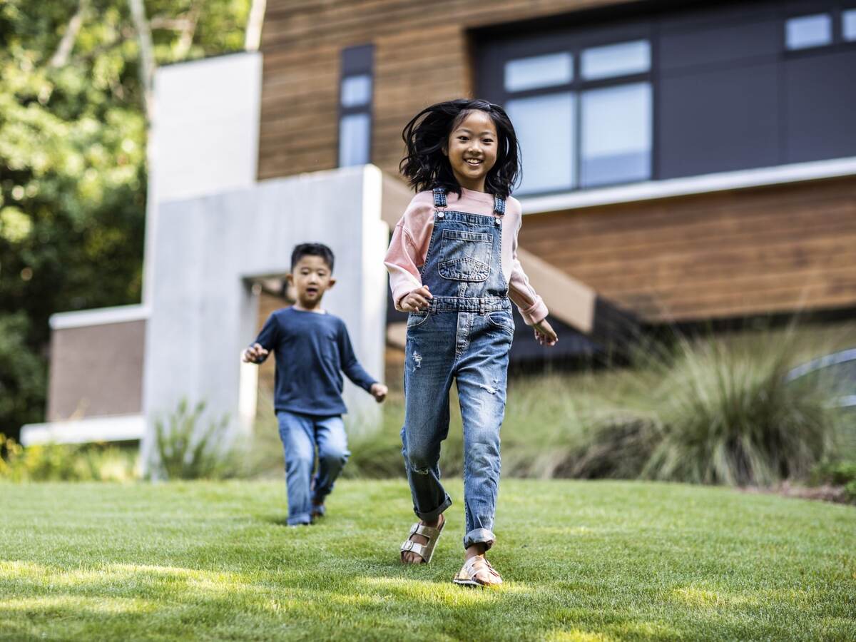 Brother and sister running in front yard of modern home.