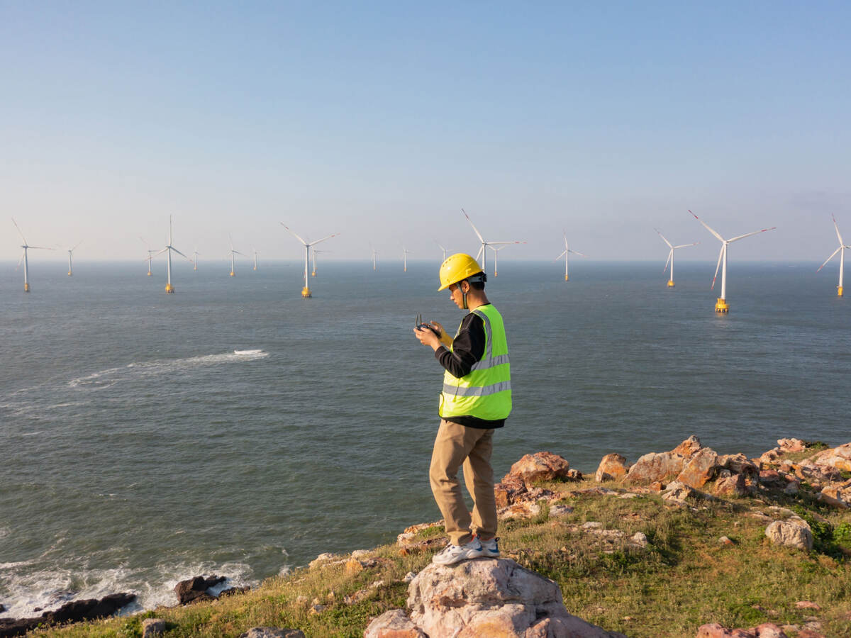 Engineer reviewing data on the coast while overlooking a wind farm at sea