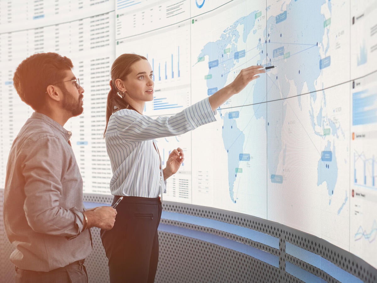 Two workers standing in front of a large monitor