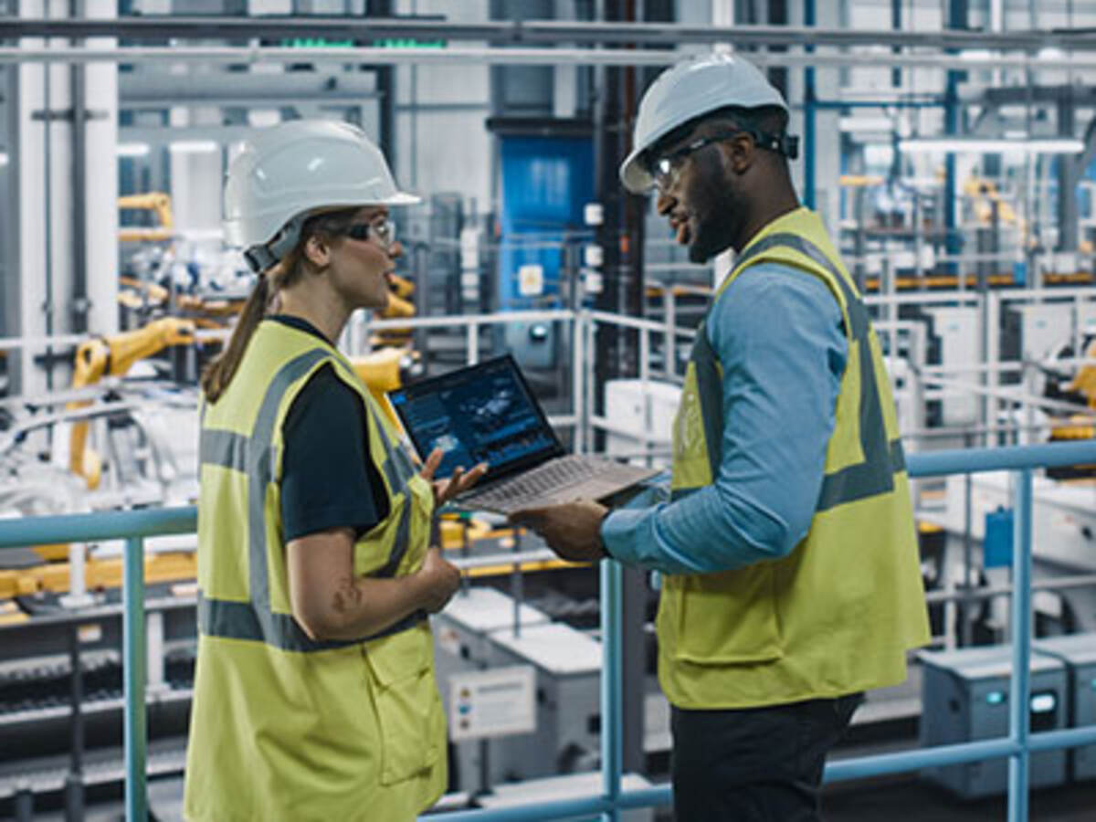 Two engineers wearing PPE and working on a laptop in a factory setting