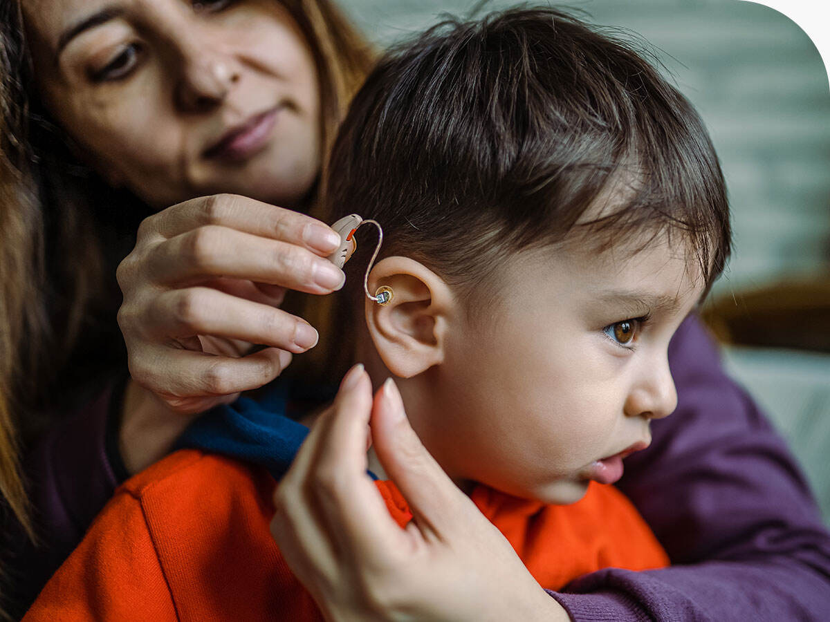 A parent placing a hearing aid onto their child's ear