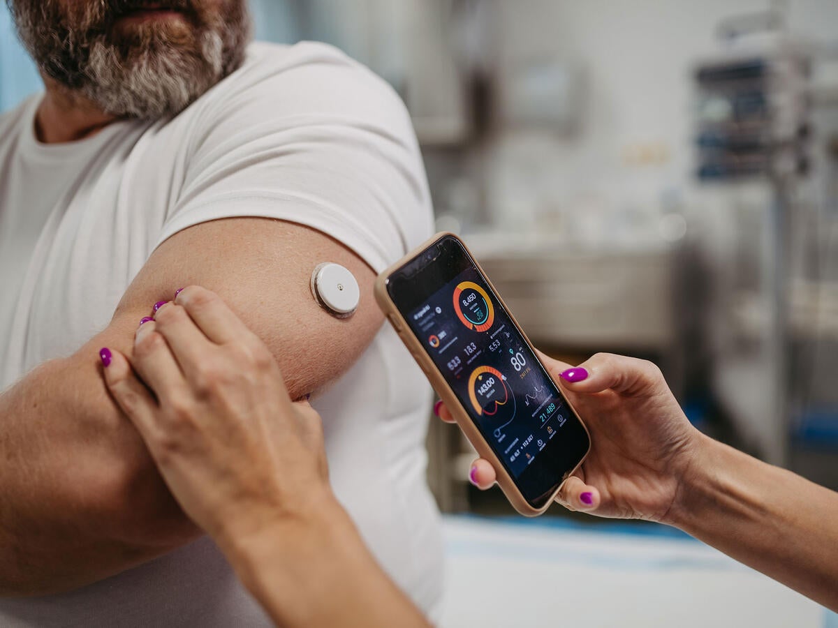 Close up a nurse using a mobile device to scan a patient's CGM