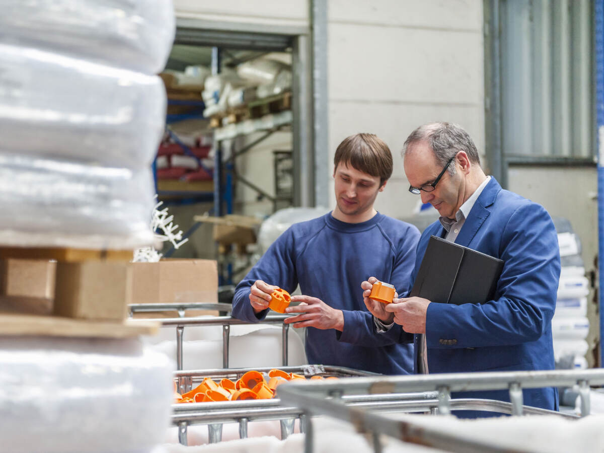 Two people inspecting a batch of orange plastic parts inside a warehouse