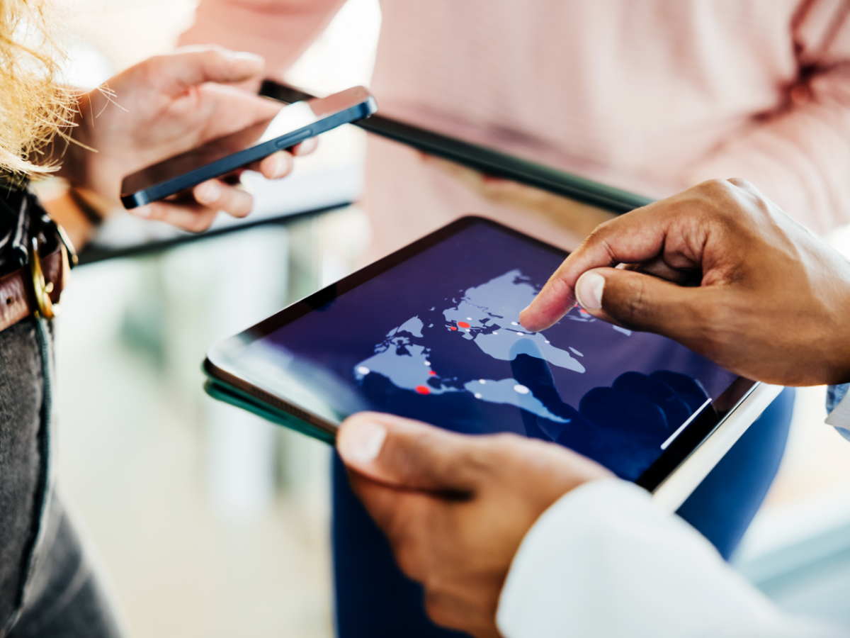 Business professionals collaborate using a digital tablet displaying a global map, indicating international reach and strategic planning