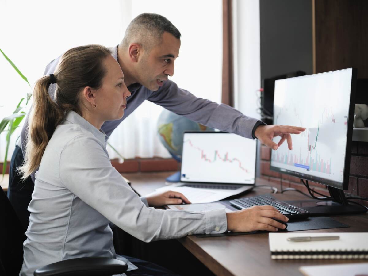 Two people, one is pointing at a chart on a monitor