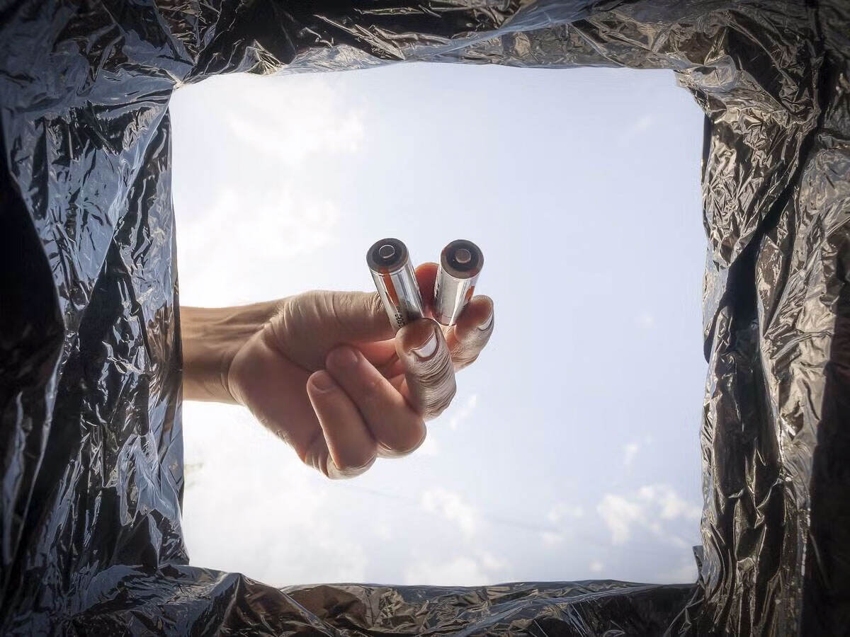 A person dropping old batteries in a bin