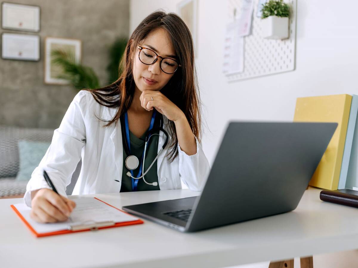 Doctor taking notes while sitting in front of a laptop