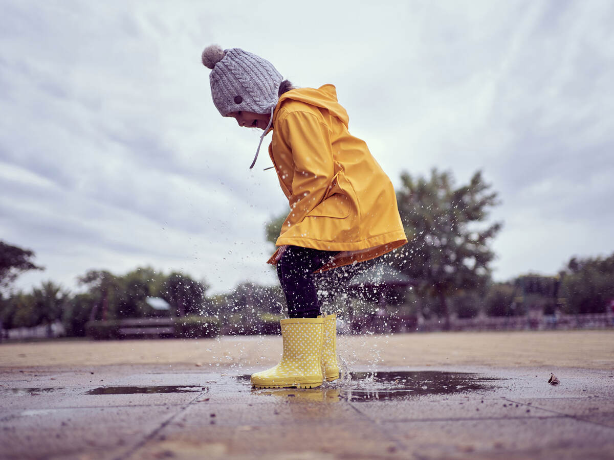 A child wearing rain gear and jumping in puddles