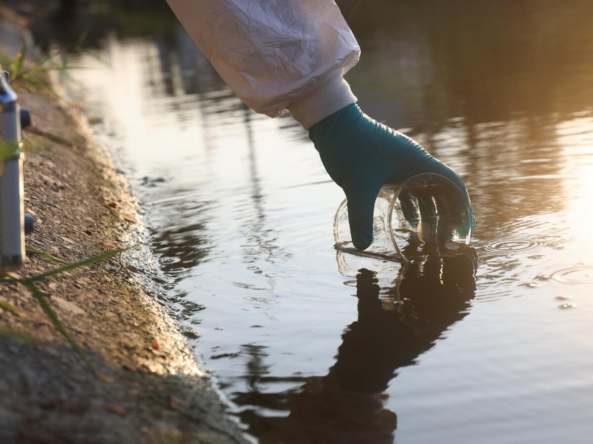 A gloved hand taking a water sample from a fresh water source
