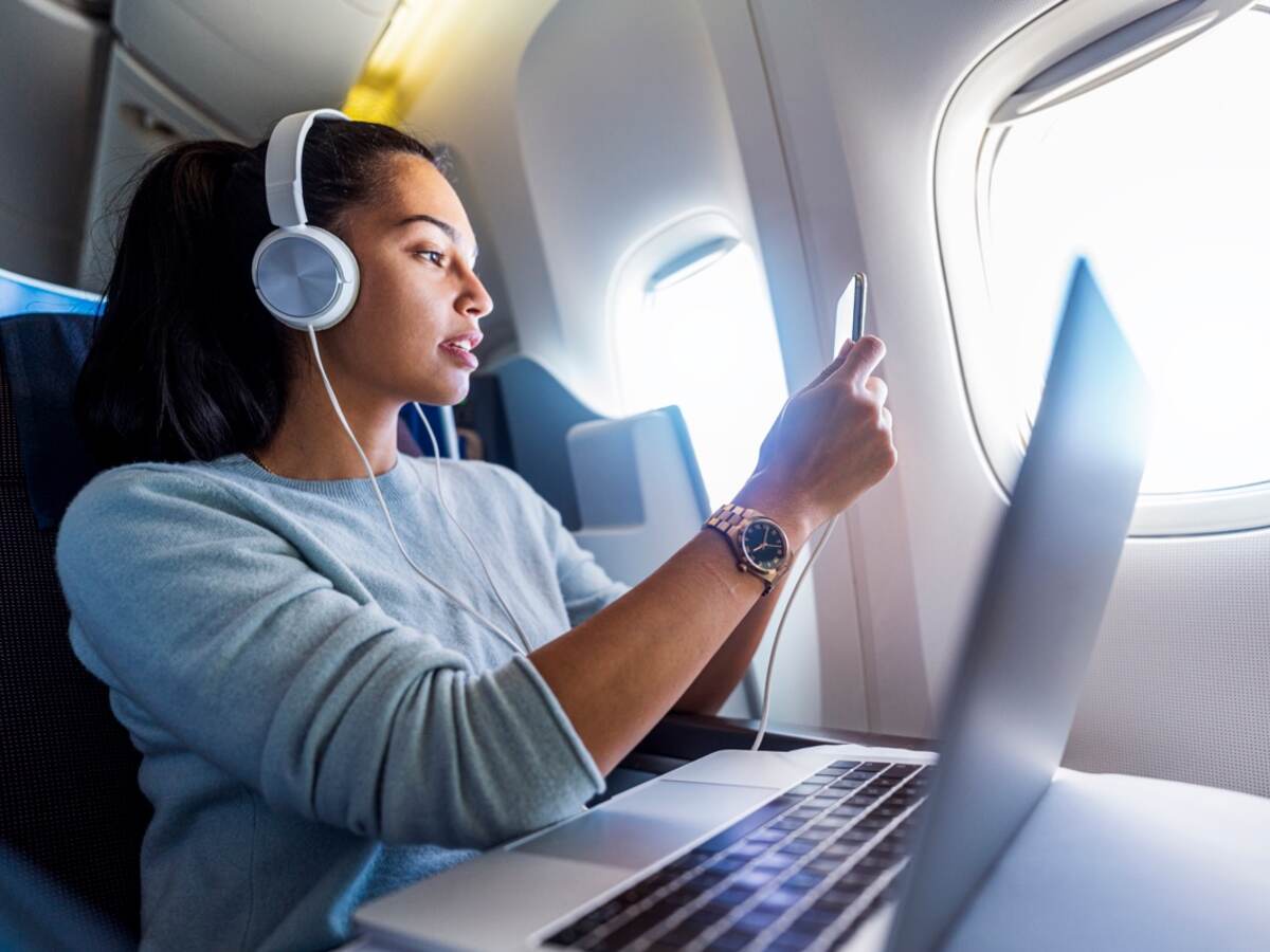 Person using mobile phone and laptop on a plane.