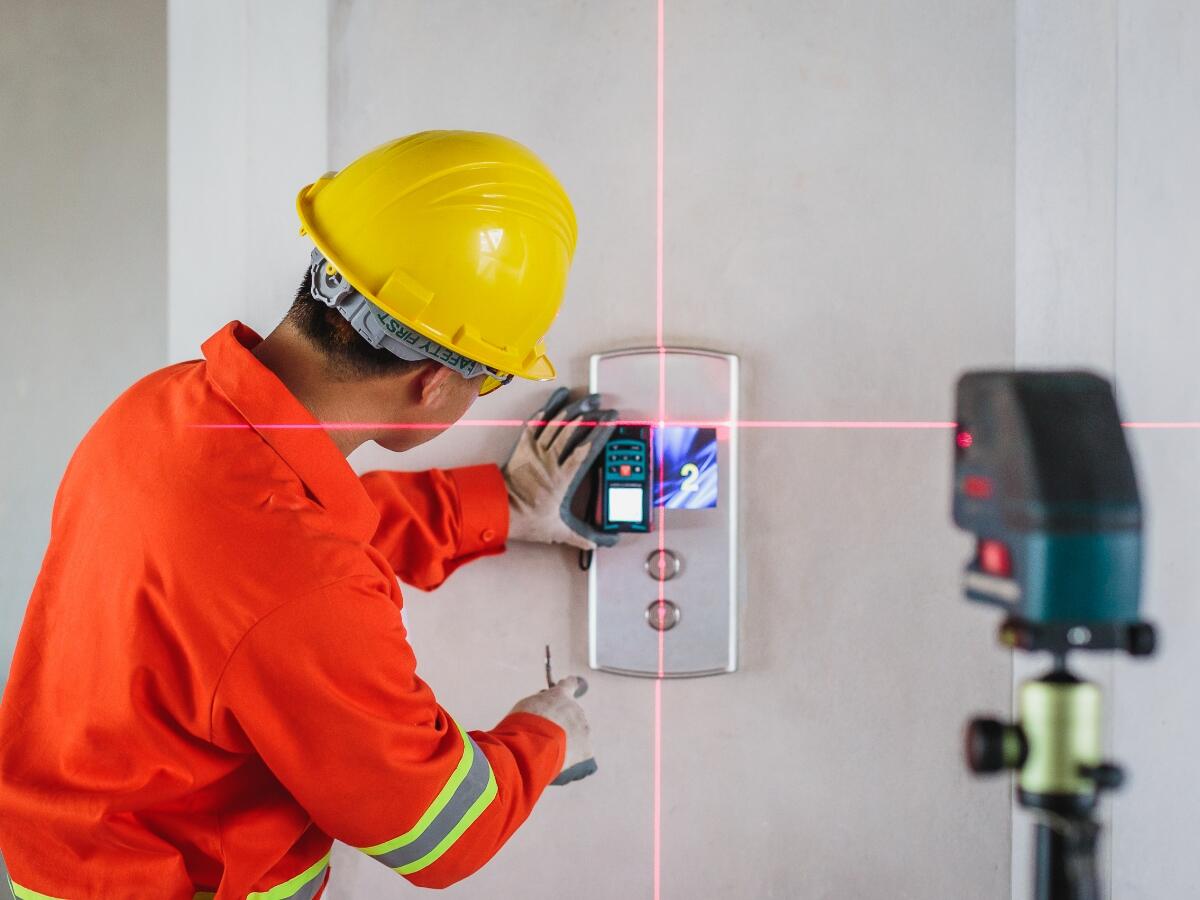 A worker in a hardhat using a laser