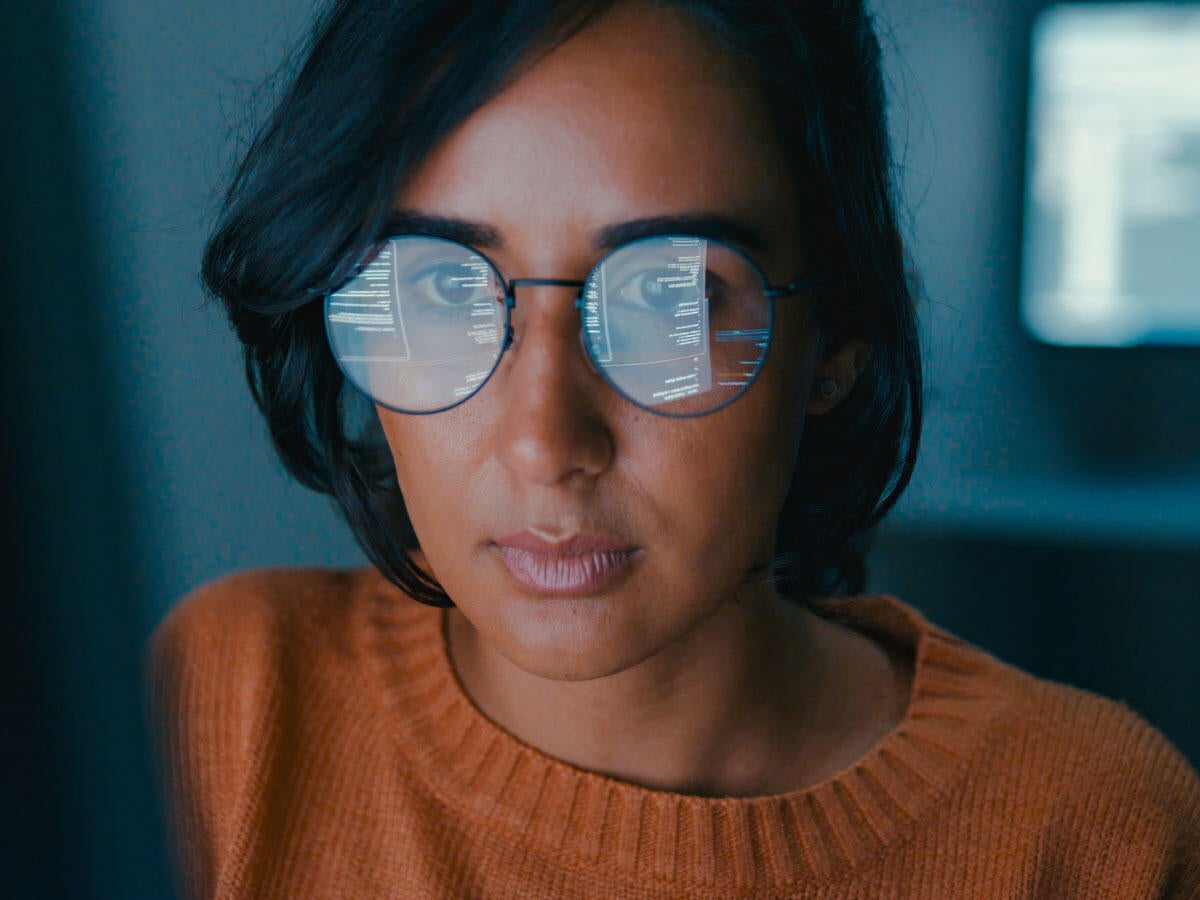 Person working on a computer with the screen reflecting in their glasses