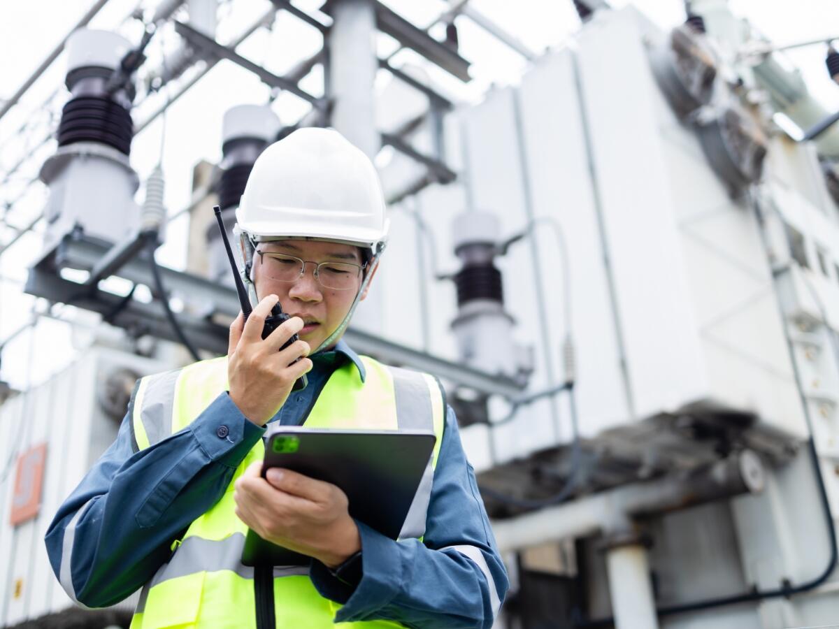 A worker wearing a hardhat and talking on a walkie talkie