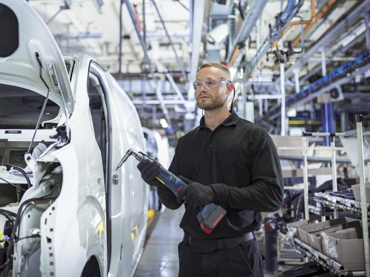 Engineer holding a drill while working on a production line in car factory