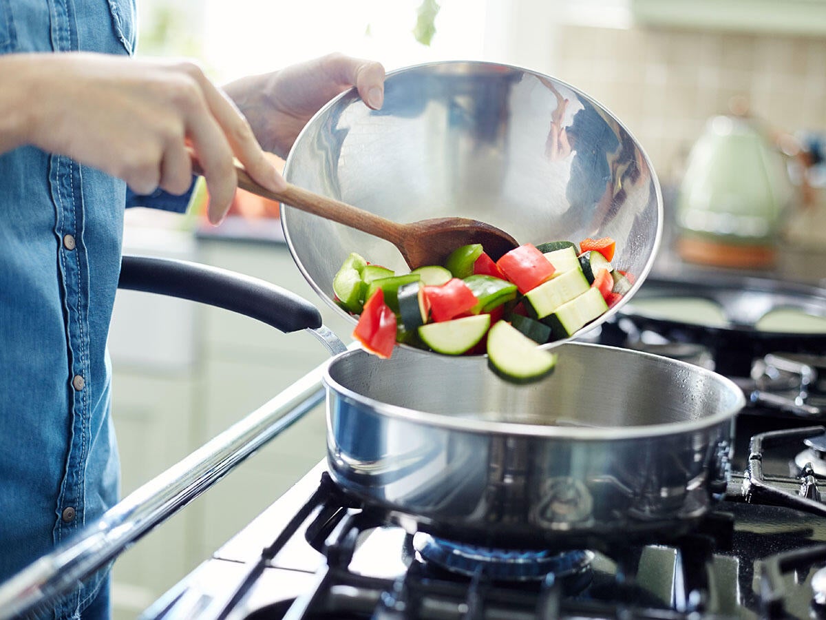 Person pouring cut vegetables into a pan on a gas stove.