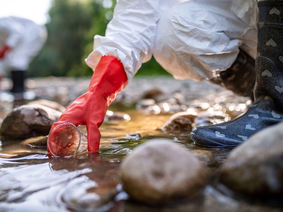 A person in PPE taking a water sample from a stream